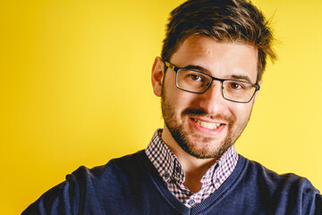 Portrait of young adult Caucasian man in front of yellow modern background wearing eyeglasses and beard with short hair looking to the camera smiling - determination concept copy space