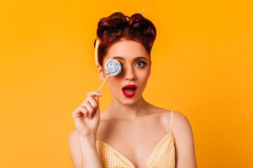 Surprised sensual woman holding lollipop. Studio shot of attractive pinup girl with sweet candy.