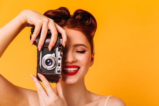 Happy pinup girl taking photos. Studio portrait of woman with camera isolated on yellow background.