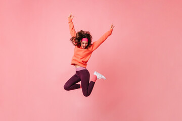 Lovely brunette girl in pink sports headband and tracksuit jumps on isolated pink background