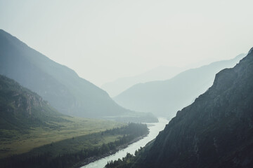 Fototapeta na wymiar Misty mountain landscape with wide mountain river. Dark green gloomy scenery with confluence of two mountain river in mist. Dark atmospheric view to confluence of great rivers in rainy weather.
