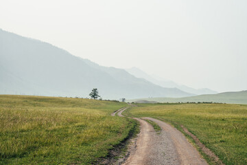 Beautiful green mountain landscape with long dirt road and big mountains in fog. Atmospheric foggy...