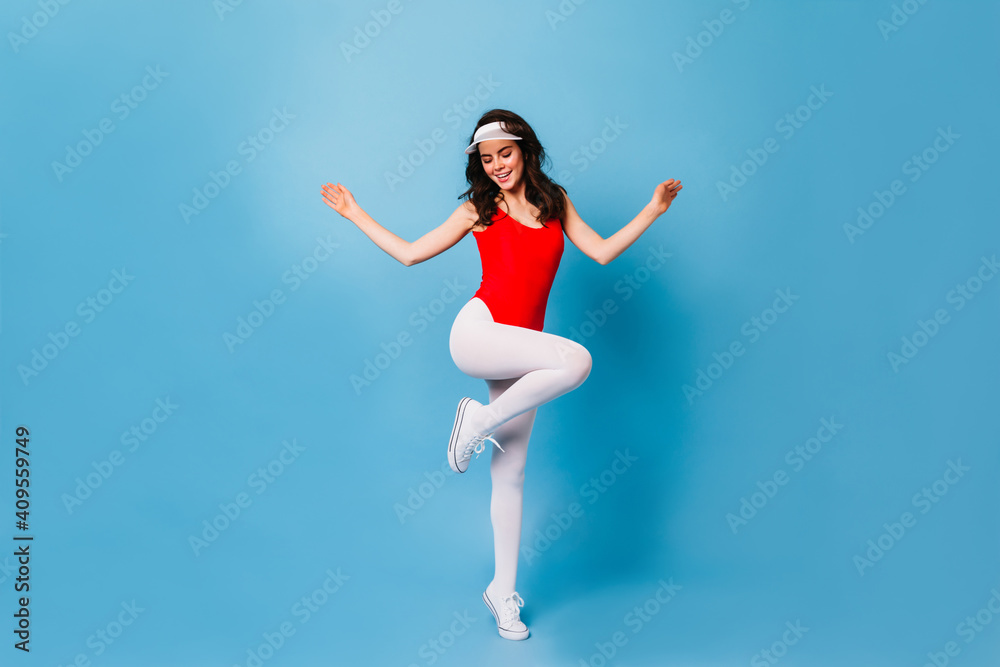 Canvas Prints Girl from 80s jumps on blue background. Full-length shot of woman in fitness bodysuit and white leggings