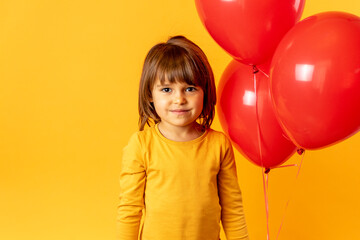 The child plays on a yellow background with red balloons. Boy holds balls, concept of fun and happiness, love