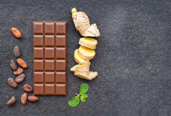 Dark chocolate with cocoa beans, with ginger root and mint on a black background