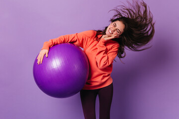 Nice girl shakes her head vigorously while holding fitball. Emotional joyful woman doing aerobics