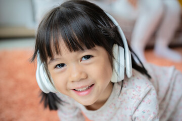 Asian little cute child girl wearing huge wireless headphones. preschool girl or kid listening to music, looking at the camera.