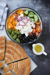 Bowl of greek salad with sliced spanakopita spiral pie, top view over dark grey stone background, vertical shot