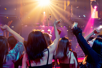 Group of people dance in disco night club to the beat of music from DJ on stage . New year night party and nightlife concept .
