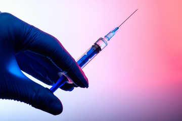 The Coronavirus Vaccine and Syringe injection in the hand in a medical glove on a pink gradient background. The concept of protection against Coronavirus infection. Healthcare and medical concept. .