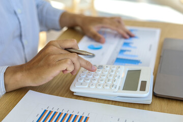 Business men are using a calculator to check the balance of the graph document of the company's...