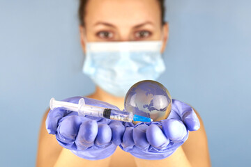 A woman in a mask and medical gloves is holding a planet earth globe and a syringe.