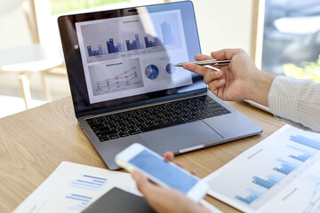 Management is checking laptop and mobile phone data for accuracy. He's looking at the company's annual income data in his office. Business management concept.