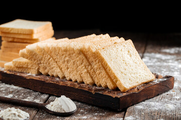 Sliced white sandwich bread on a wooden cutting board with flour