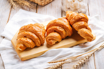 Three french croissants on the wooden cutting board decorated with wheat and napkin