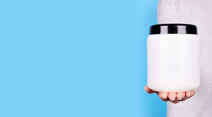 Hand with white cosmetic bottle on blue background.