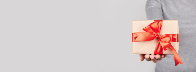 Hand with giftbox with red ribbon on grey background.