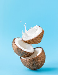 Cracked coconut with splashes of milk on blue background - obrazy, fototapety, plakaty