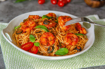 Pasta in tomato sauce with shrimps, olives, basil and garlic on a beautiful plate. 