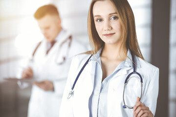 Professional beautiful woman-doctor with a stethoscope is standing straight in a sunny clinic. Young doctors at work in a hospital. Perfect medicine concept