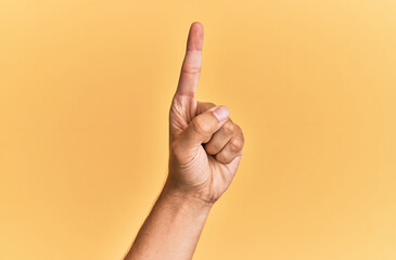 Arm and hand of caucasian man over yellow isolated background counting number one using index finger, showing idea and understanding