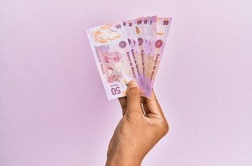 Hispanic hand holding 50 mexican pesos  banknotes over isolated pink background.