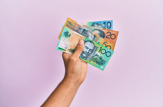 Hispanic hand holding australian dollars banknotes over isolated pink background.