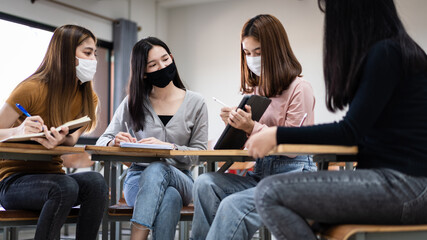 Group of diverse international students wearing protective  masks and talking, discussing project, sitting at desk in the classroom at the university