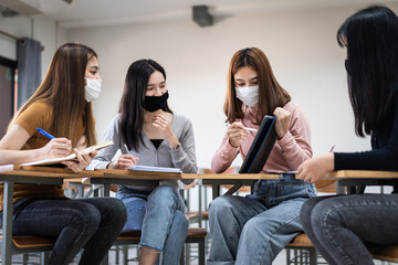 Group of diverse international students wearing protective  masks and talking, discussing project, sitting at desk in the classroom at the university