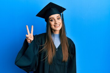 Beautiful brunette young woman wearing graduation cap and ceremony robe showing and pointing up...
