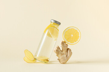 Bottle of infused water with ginger and lemon over light yellow background.