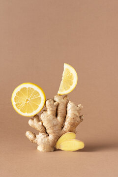Composition of fresh ginger root and lemon over light brown background.