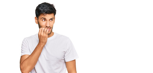 Young handsome man wearing casual white tshirt looking stressed and nervous with hands on mouth biting nails. anxiety problem.