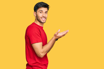 Young handsome man wearing casual red tshirt pointing aside with hands open palms showing copy space, presenting advertisement smiling excited happy