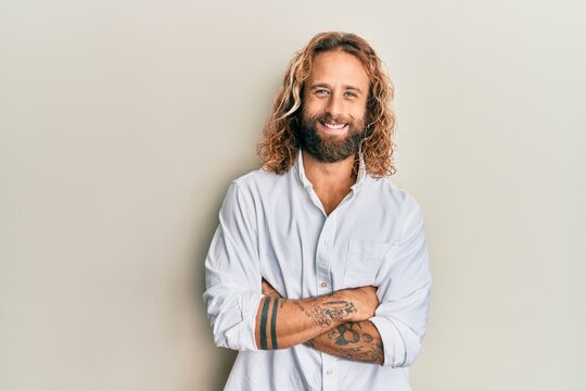 Handsome man with beard and long hair wearing casual white shirt happy face smiling with crossed arms looking at the camera. positive person.