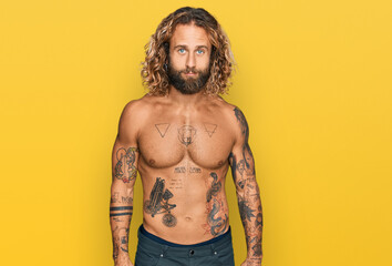 Fototapeta premium Handsome man with beard and long hair standing shirtless showing tattoos relaxed with serious expression on face. simple and natural looking at the camera.