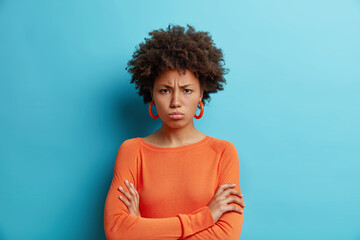 Horizontal shot of dark skinned offended woman with Afro hair keeps arms folded has offensive...