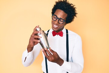 Handsome african american bartender man with afro hair preparing cocktail mixing drink with shaker...
