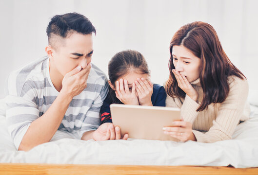 asian family watching horror movie with tablet in bed