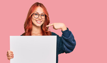 Young redhead woman holding blank empty banner pointing finger to one self smiling happy and proud