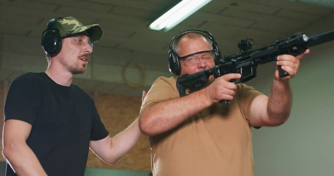 A man learns how to shoot a rifle at the shooting range. The instructor shows the trainee the correct shooting position.
