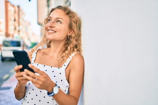 Young beautiful caucasian woman with blond hair smiling happy outdoors using smartphone