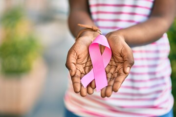Hands of african american girl holding pink breast cancer ribbon at the park.