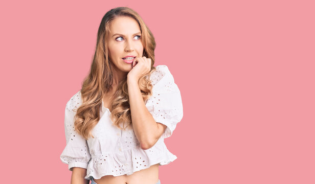 Young caucasian woman with blond hair wearing elegant summer tshirt looking stressed and nervous with hands on mouth biting nails. anxiety problem.