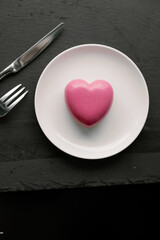 Delightful, luxury, romantic mousse cake in the form heart served on a white plate.. Valentine's Day on February 14. Dark Background. Flat lay top view