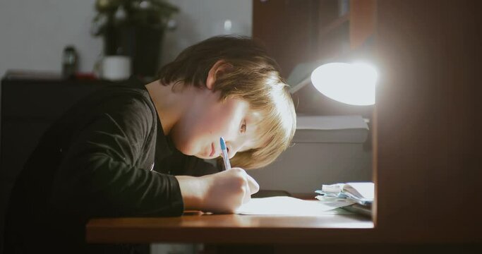 Homeschooling concept. A school-age child doing homework at home under the light of lamp.
