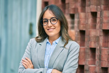 Young hispanic businesswoman with arms crossed smiling happy at the city