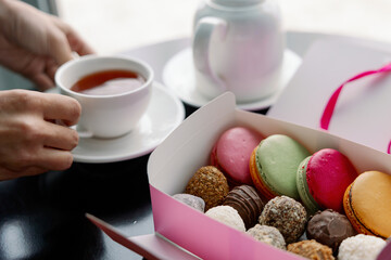 Composition with colorful macaroons, sweets truffle and custard dessert shu in paper box teapot and up of tea on dark background. Gift sets of sweets for Valentine's Day, February 14 and March 8.