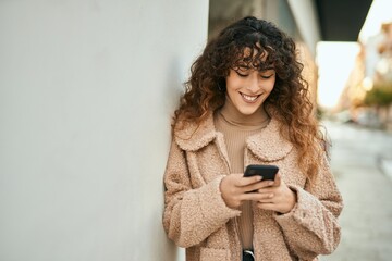 Young hispanic woman smiling happy using smartphone at the city