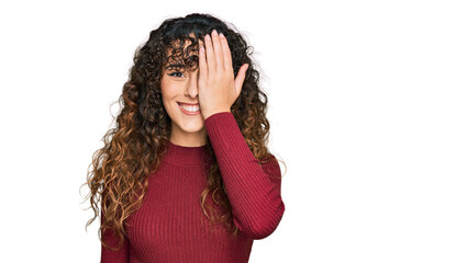 Young hispanic girl wearing casual clothes covering one eye with hand, confident smile on face and surprise emotion.